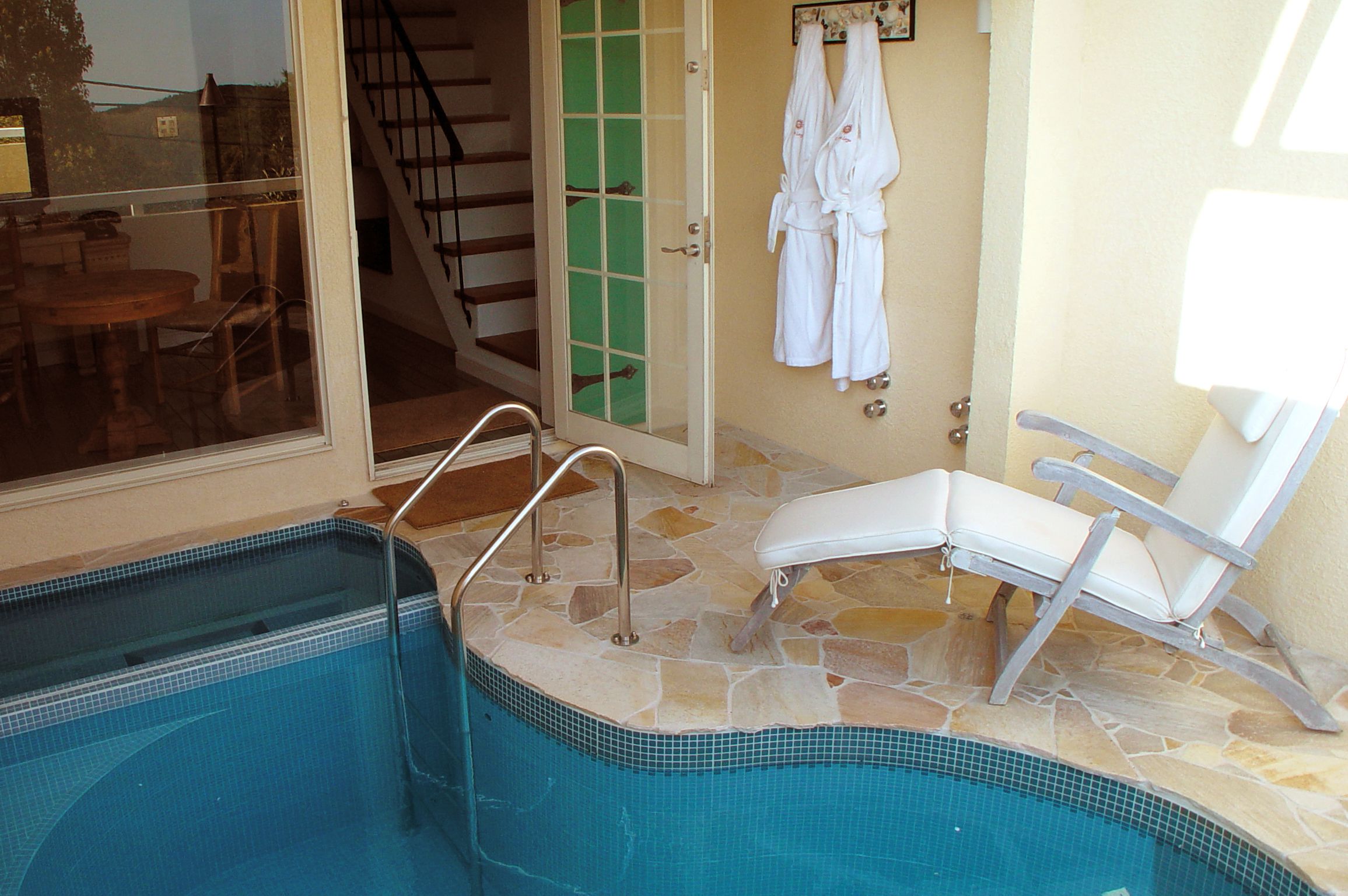 A swimming pool with a glass door, a lounge chair, and a set of stairs leading to an upper level.