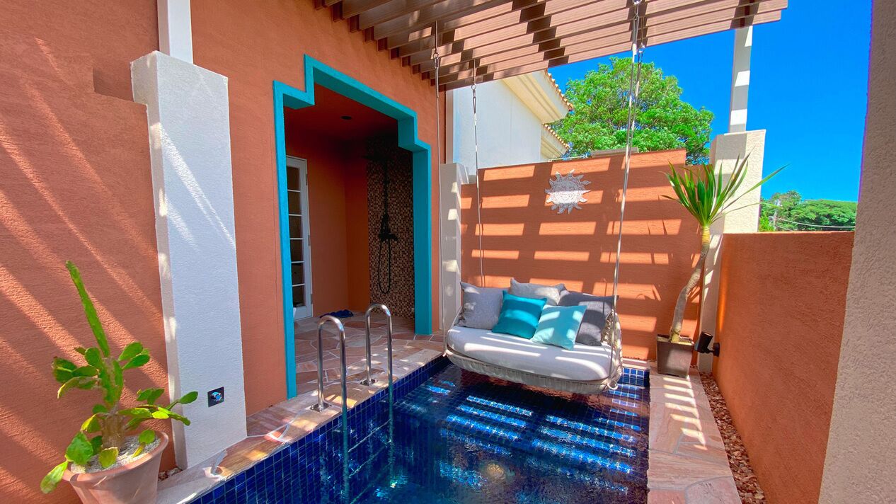 A poolside area with a sofa, a potted plant, and a clear blue sky.