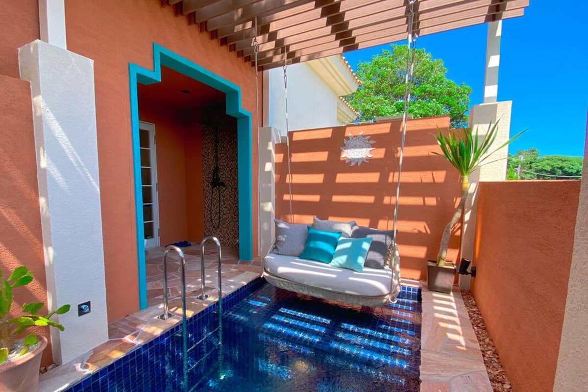 A poolside area with a sofa, a potted plant, and a clear blue sky.