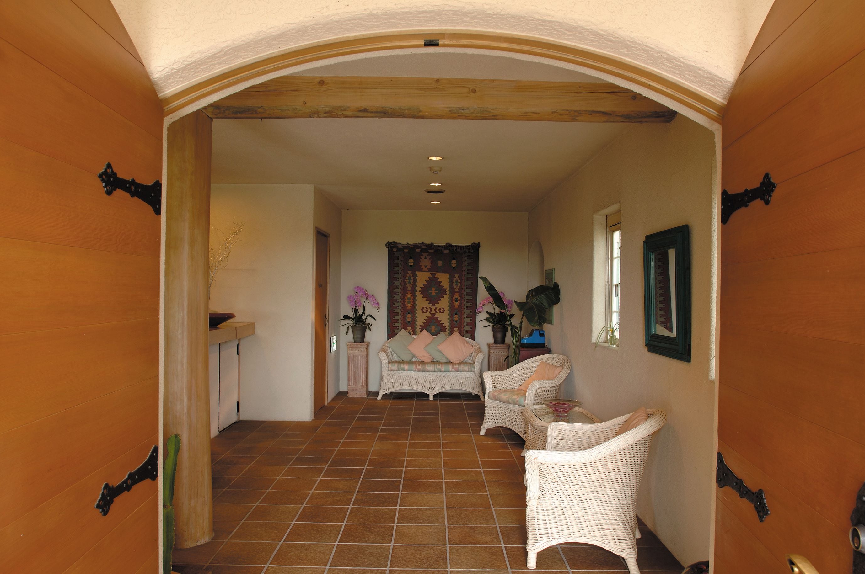 A hallway with a tiled floor, a sofa, two wicker chairs, a small table, and a decorative wall hanging.