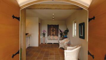 A hallway with a tiled floor, a sofa, two wicker chairs, a small table, and a decorative wall hanging.