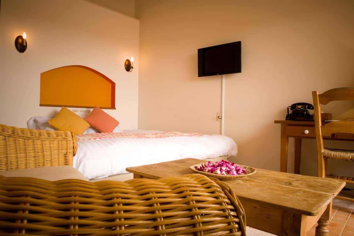 A hotel room with a bed, wicker furniture, a wooden table, and a television mounted on the wall.
