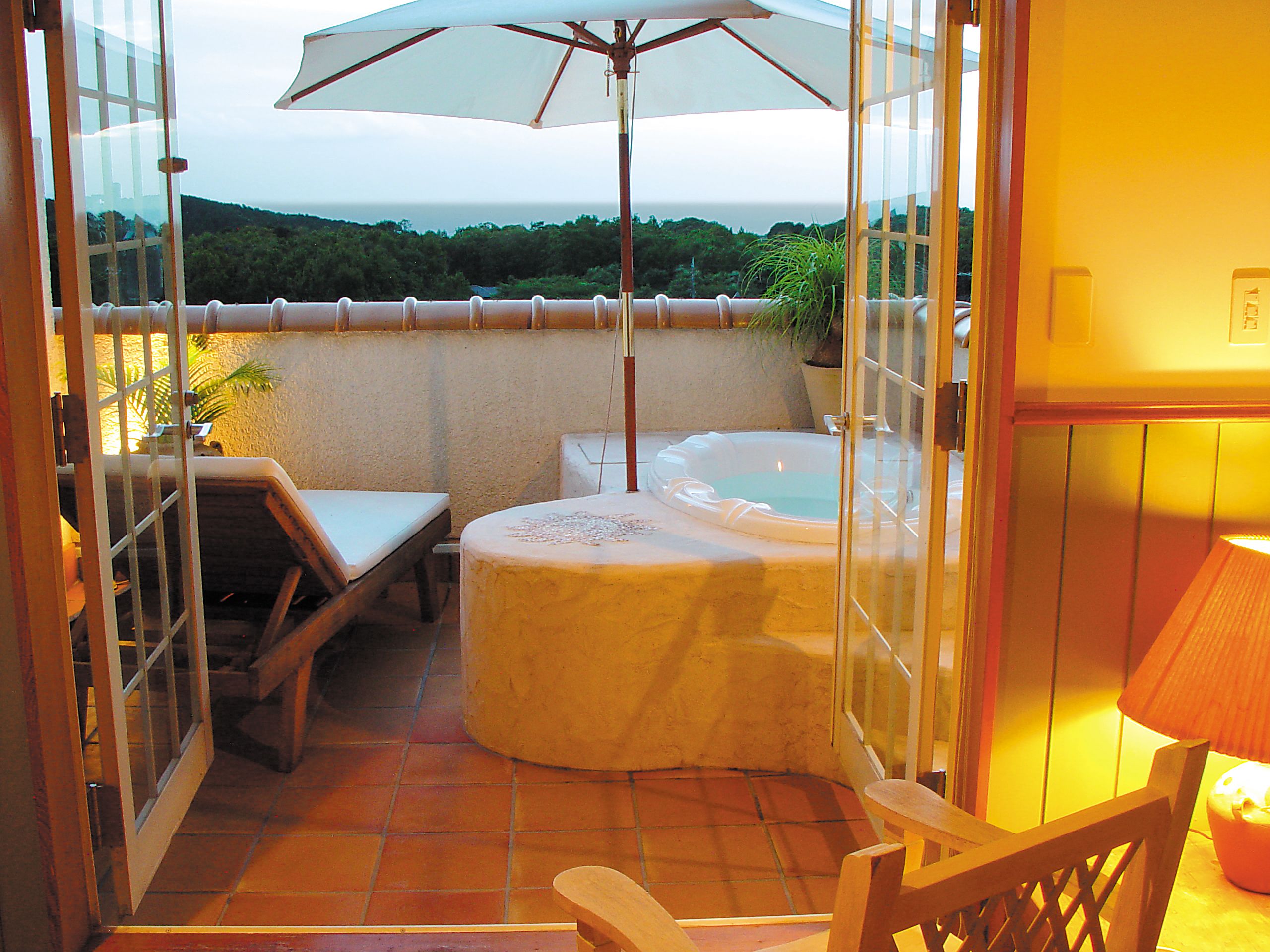 A balcony with a hot tub, a table, and an umbrella.