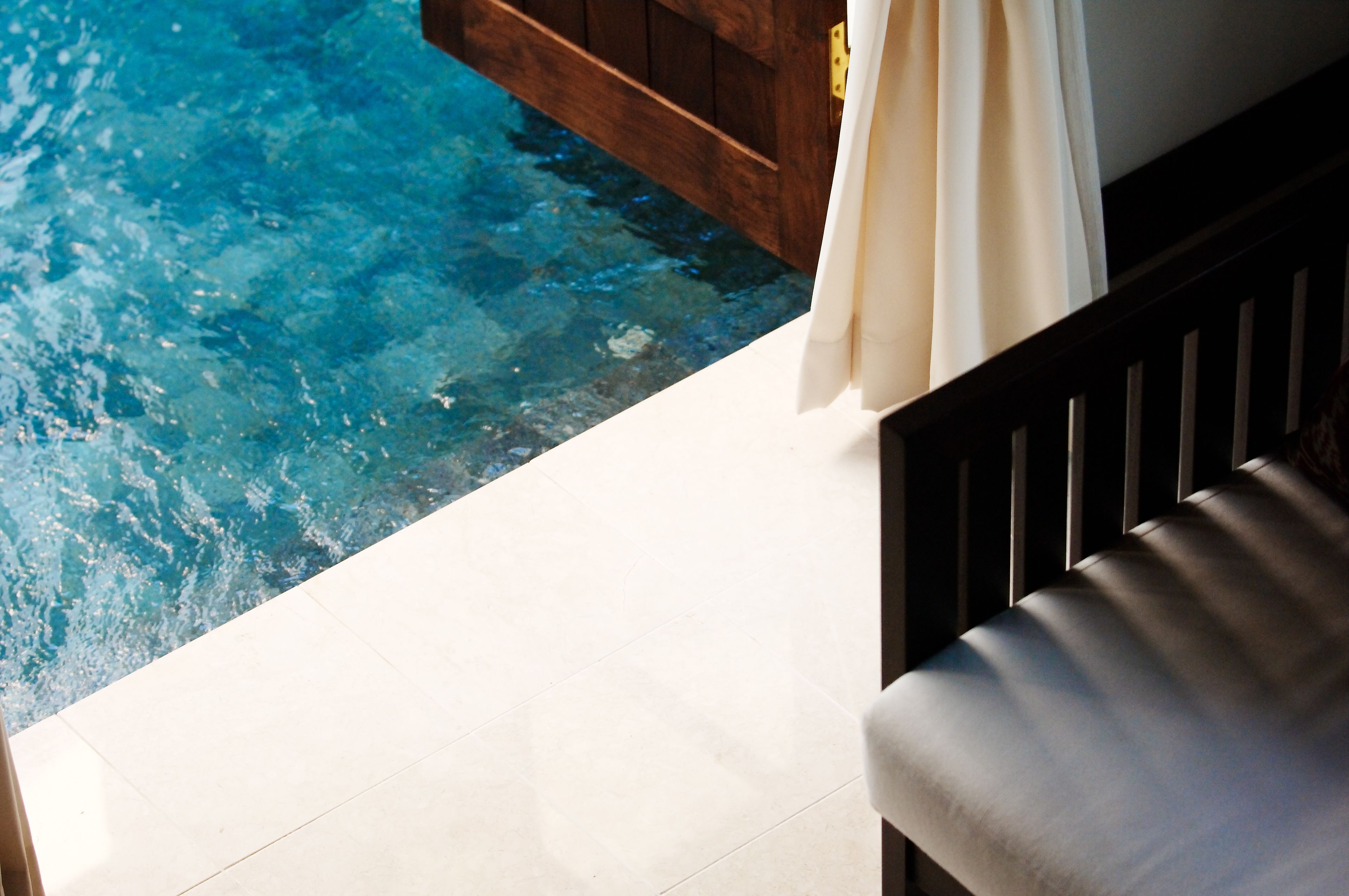 A poolside area with a wooden deck and a white tiled floor.