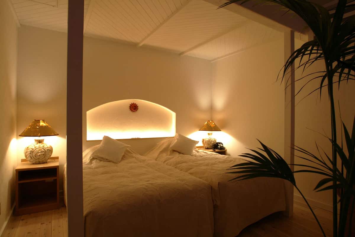 A bedroom with two beds, a nightstand with a lamp, and a wall-mounted light fixture.