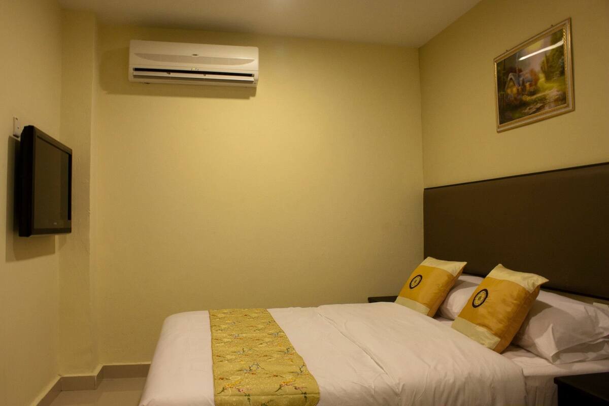 A hotel room with a bed, a television, an air conditioning unit, and a painting on the wall.