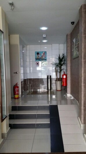 A hotel lobby with tiled floors, a fire extinguisher, a potted plant, and a fire alarm. - SohoTown Hotel (Kuala Lumpur)