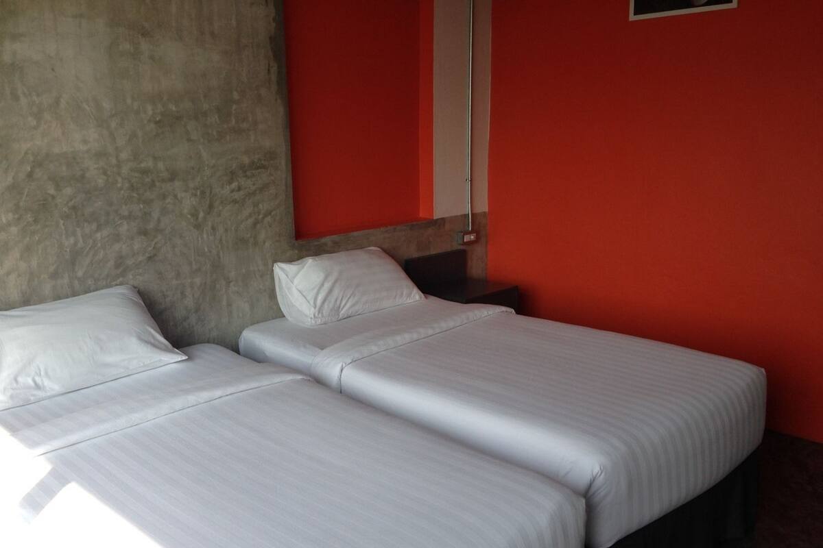 Ein Zimmer mit zwei Betten, einer roten Wand und einer Wand mit Betonoptik.