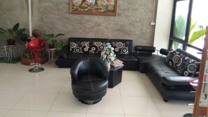 A living room with a black sofa, a red chair, and a painting on the wall. - Pornsiri Hotel Sisaket (Sisaket)