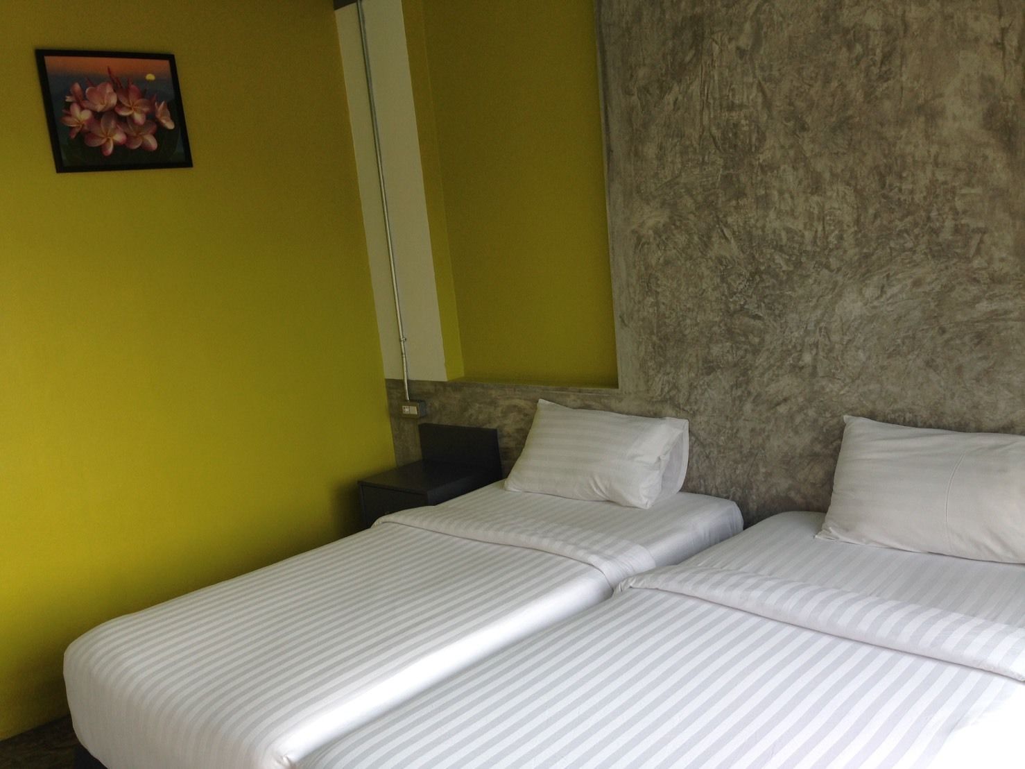 A hotel room with two beds, a nightstand, a lamp, and a wall-mounted picture.
