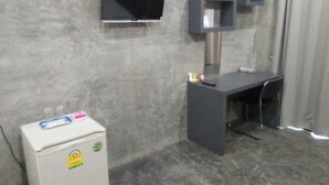 A room with a grey concrete wall, a white refrigerator, a desk with a chair, and a mounted television. - Pornsiri Hotel Sisaket (Sisaket)