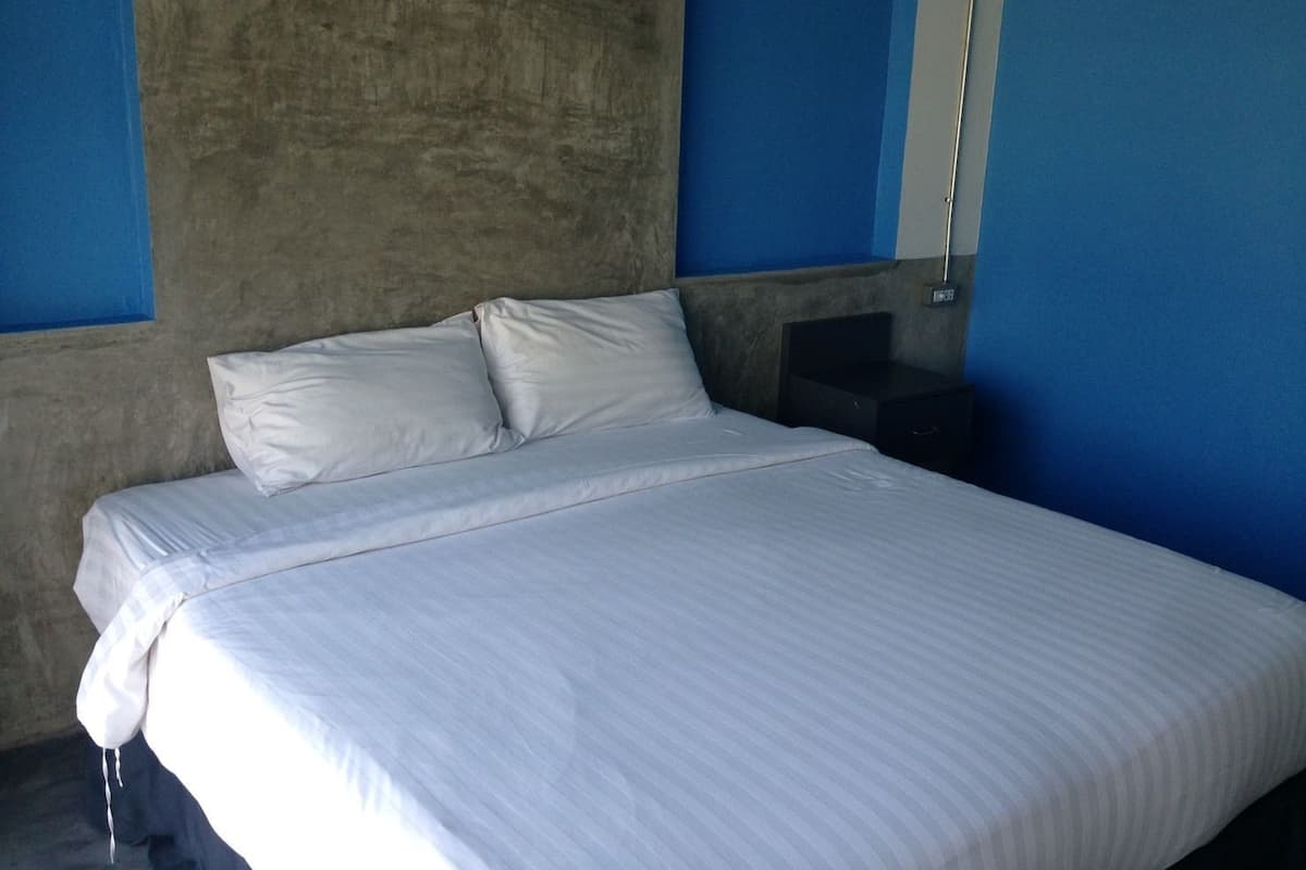 Ein Bett mit weißer Bettwäsche in einem Zimmer mit blauen Wänden und einer Betonwand als Blickfang.