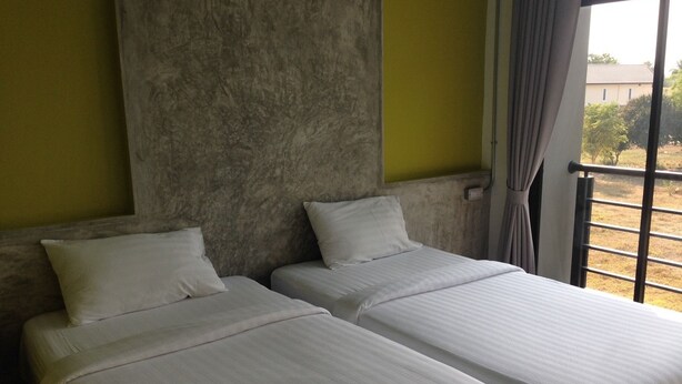 A room with two beds, a large window with a view of the outdoors, and a textured wall. - Pornsiri Hotel Sisaket (Sisaket)