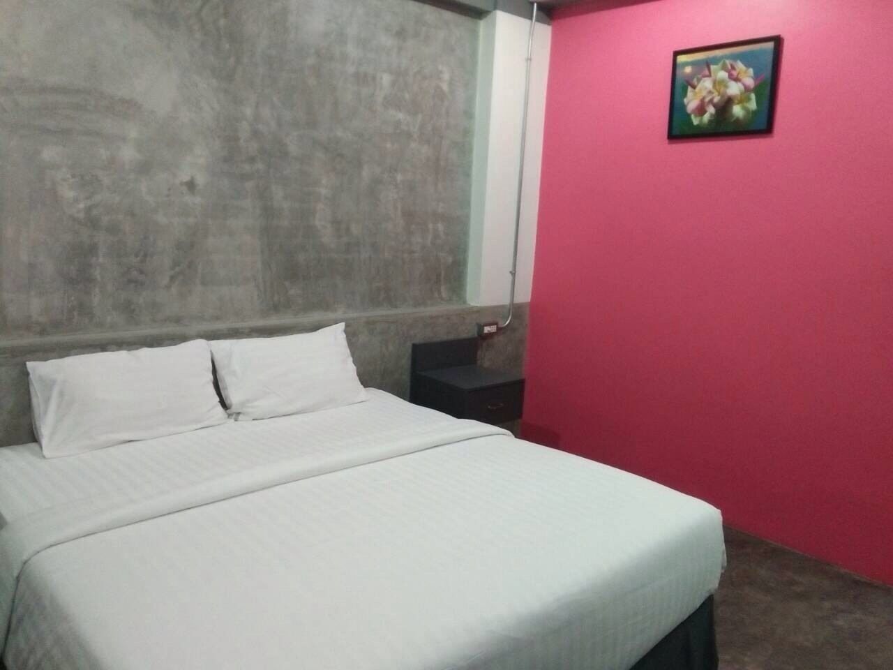 Una habitación con una cama, una mesita de noche, una pared rosa y un cuadro enmarcado.