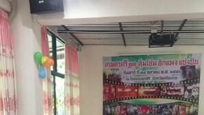 A conference room with a long table, white chairs, and a pink tablecloth. There is a banner on the wall with text and images, and balloons are visible on the windowsill. - Pornsiri Hotel Sisaket (Sisaket)