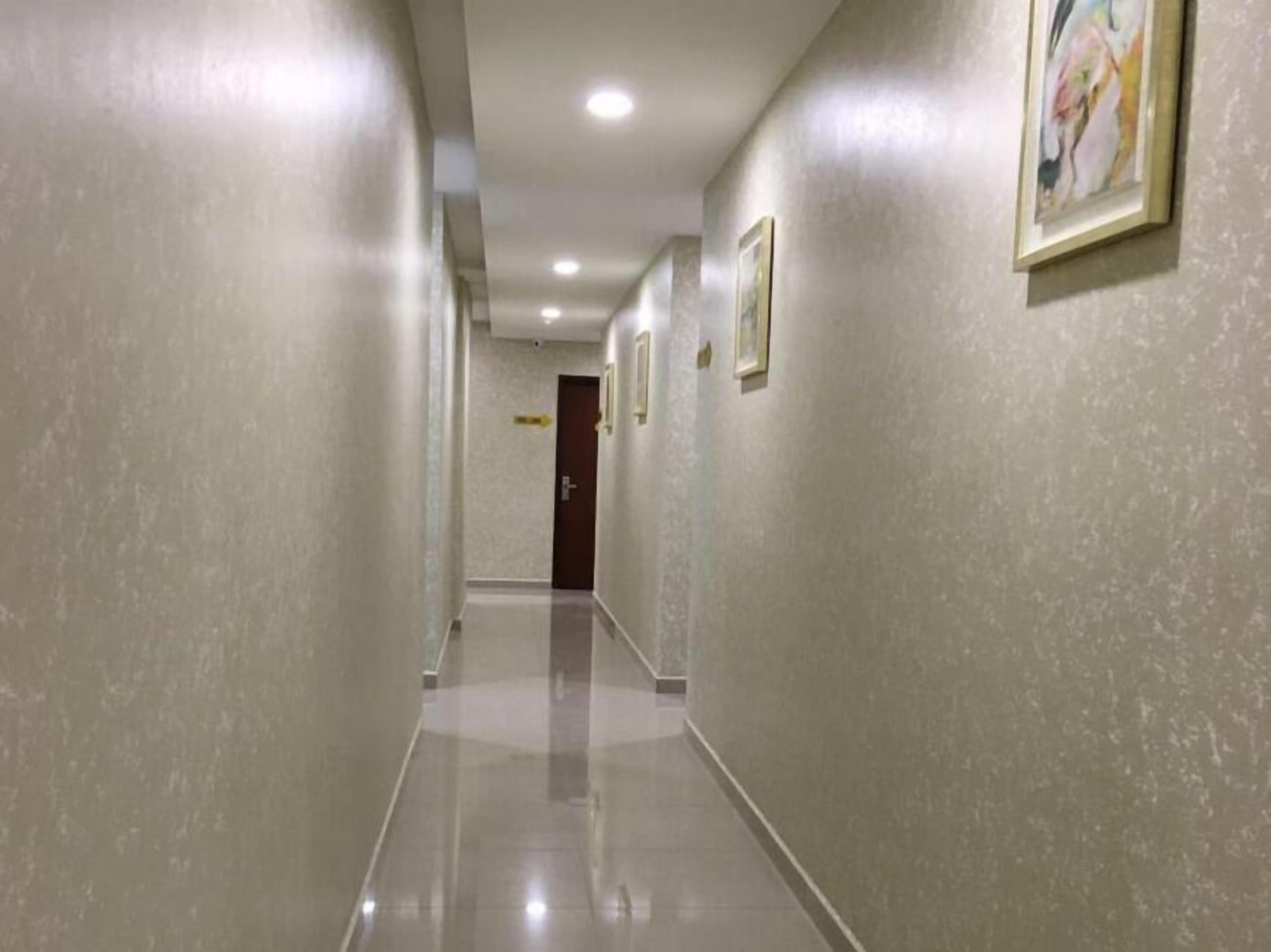 A long, narrow hallway with light-colored walls and a shiny floor, leading to a door at the end.