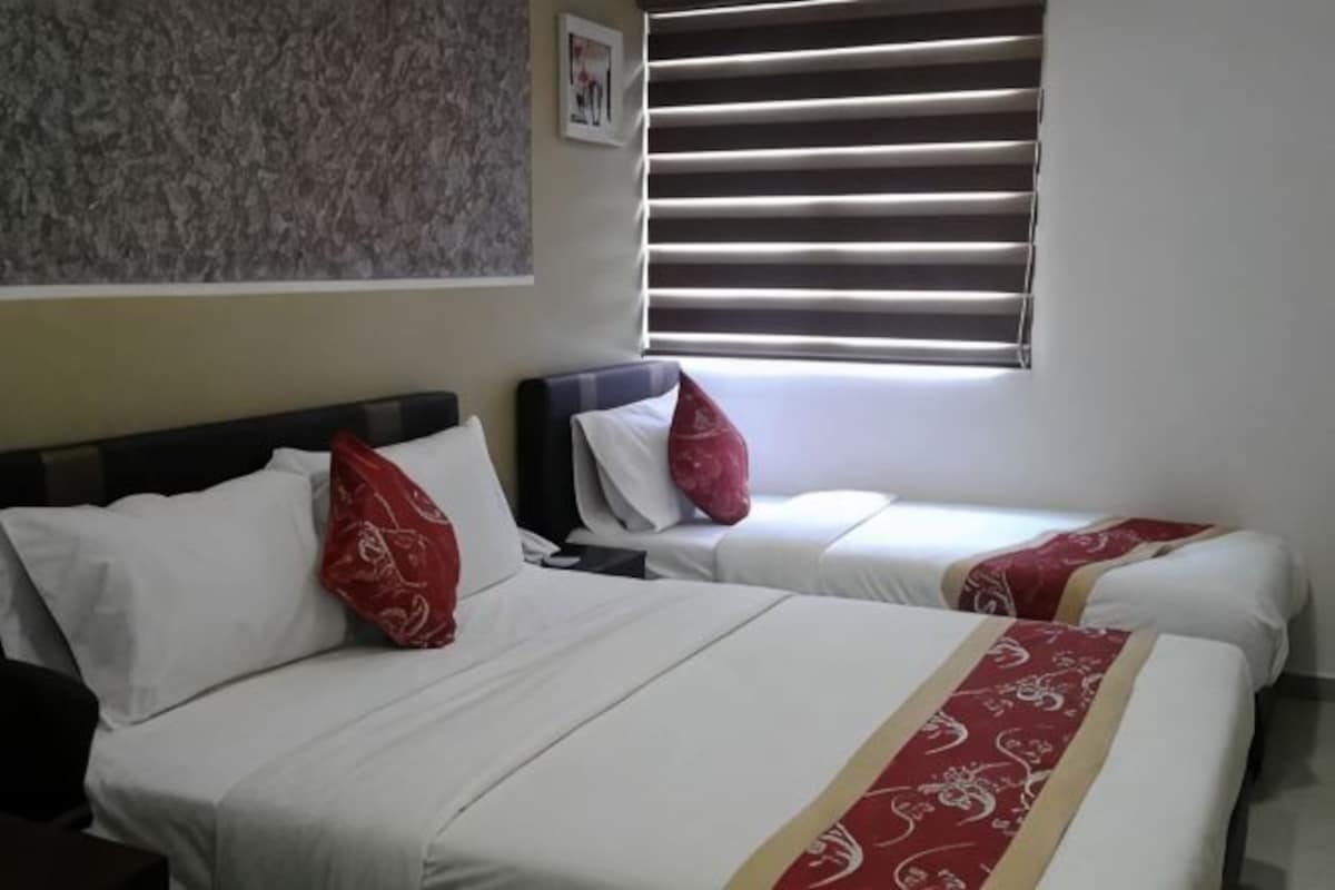 Habitación con dos camas, cada una con ropa blanca y detalles rojos, una ventana con persianas y una pared con un diseño texturizado.