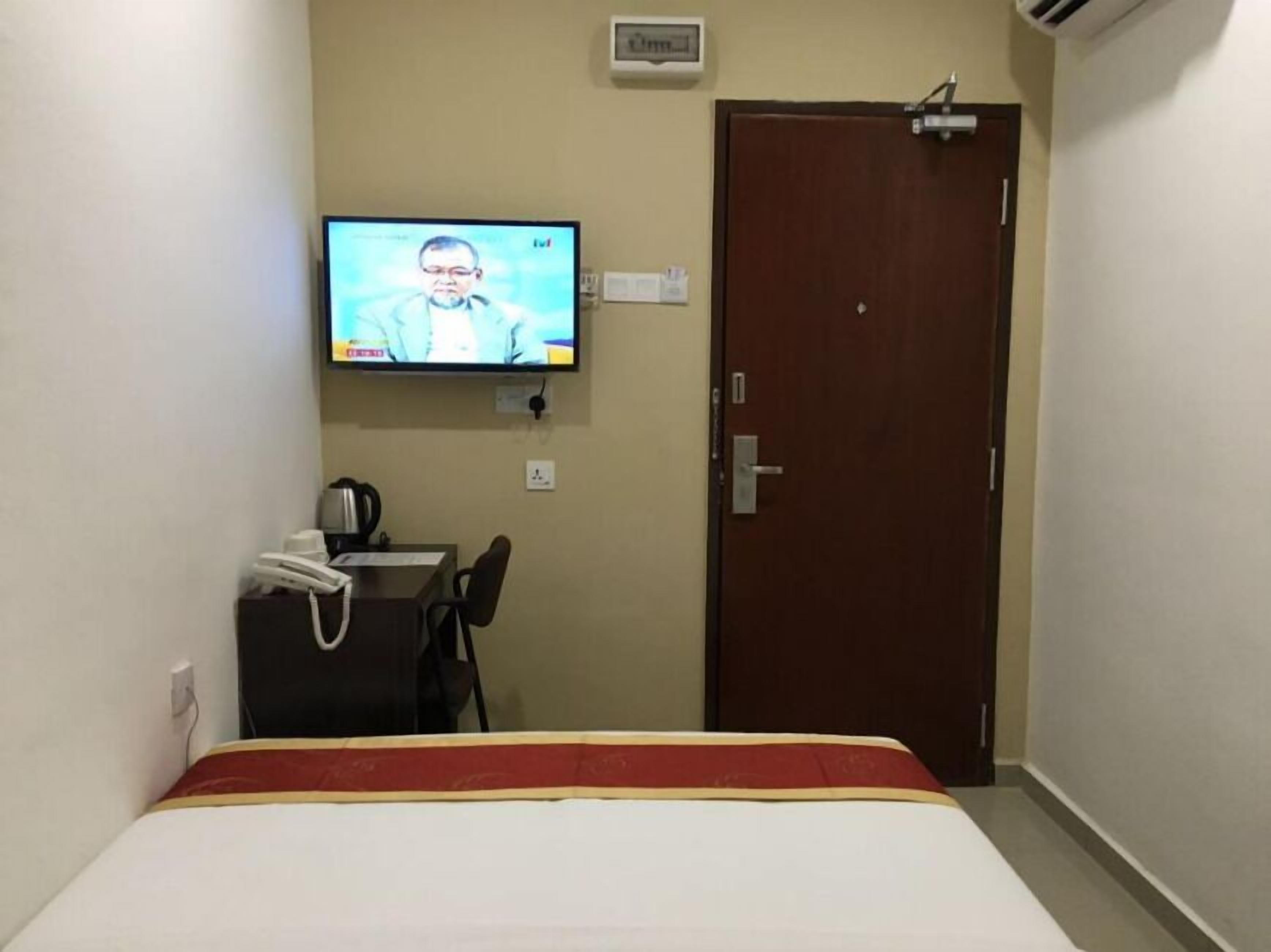 A hotel room with a bed, a desk with a chair, a television mounted on the wall, and a door.