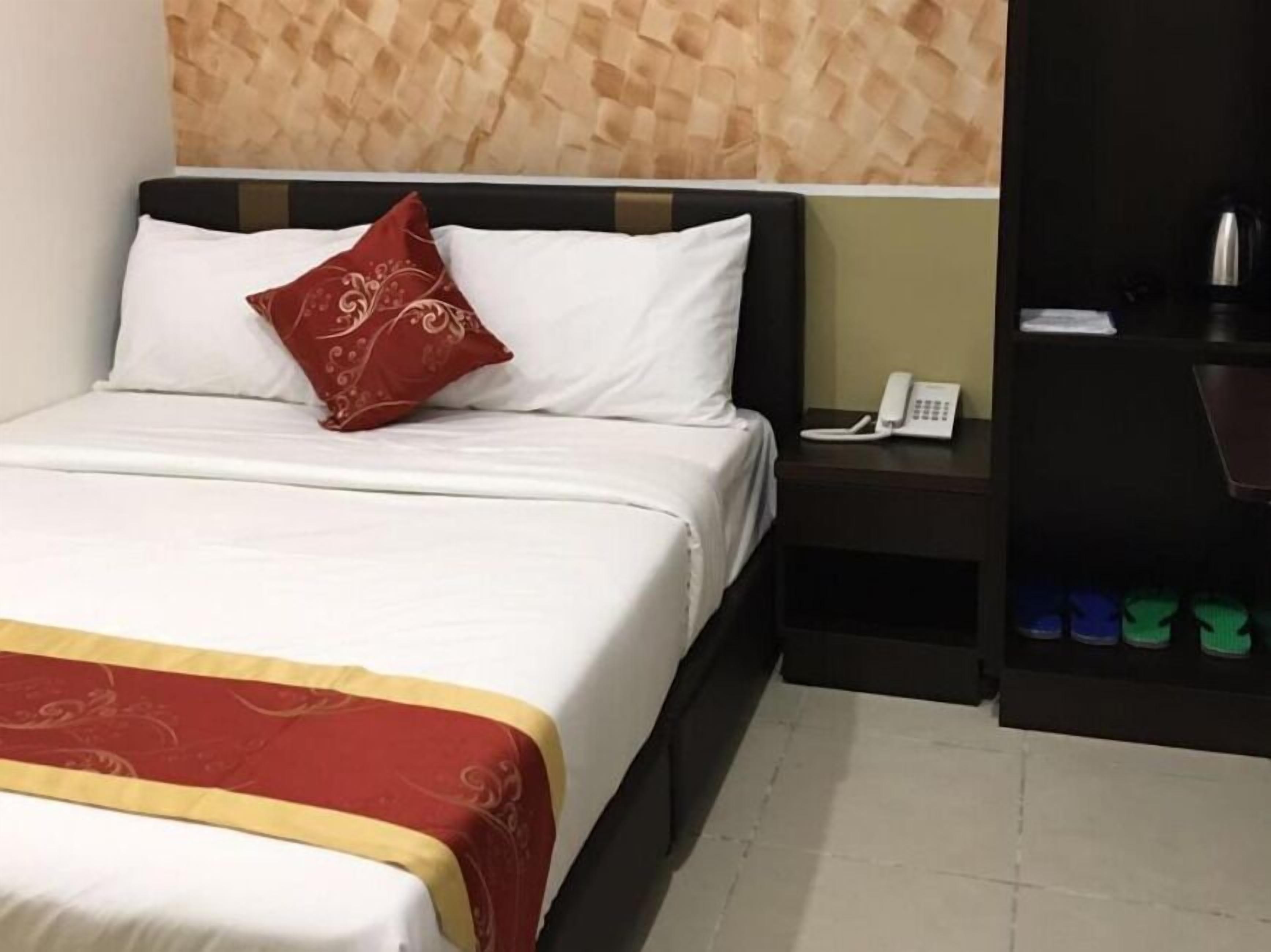 A hotel room with a bed, a telephone, and a shoe rack with multiple pairs of shoes.