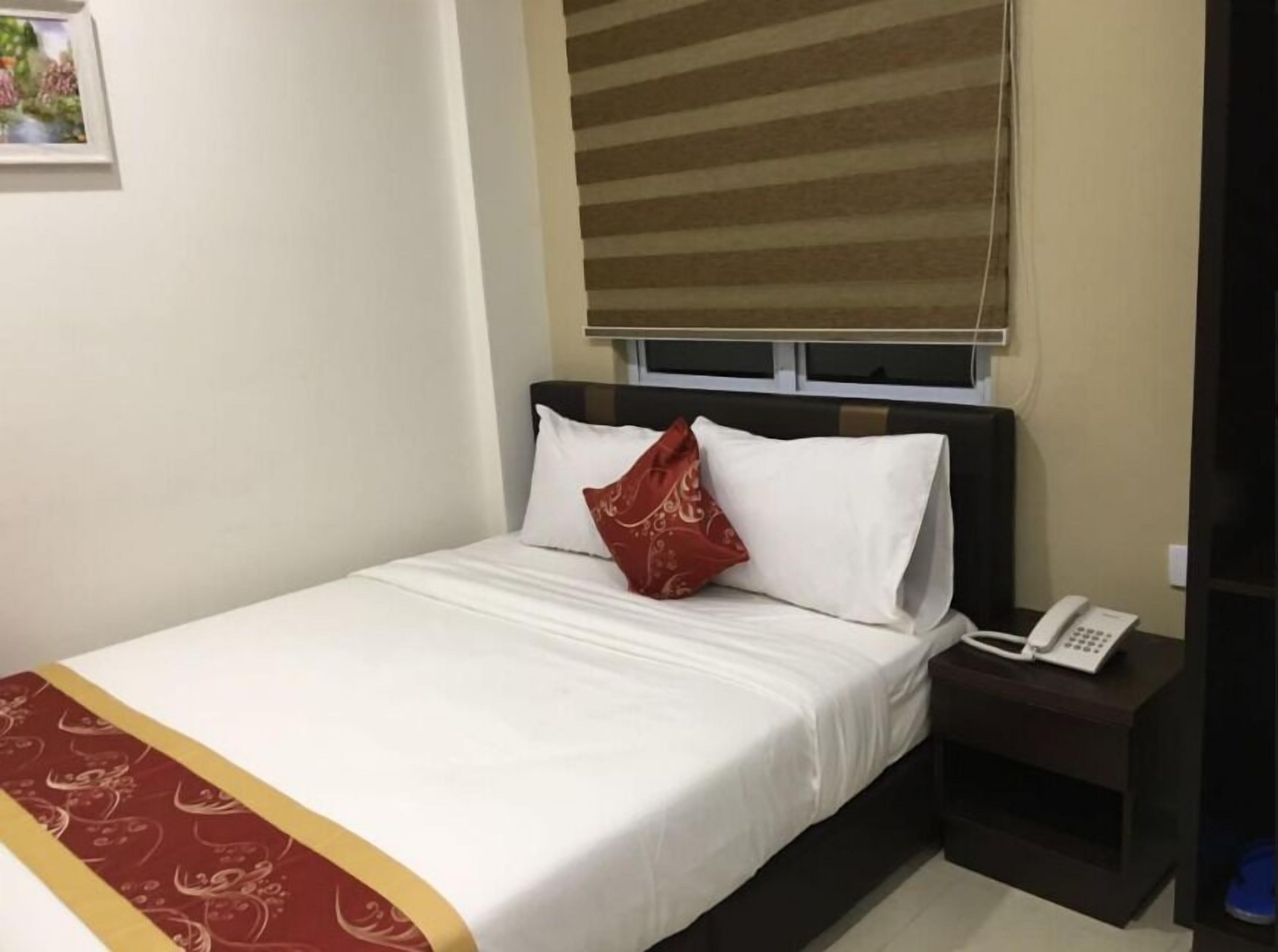 Une chambre d’hôtel avec un lit, une table de chevet avec un téléphone et une fenêtre avec des stores.