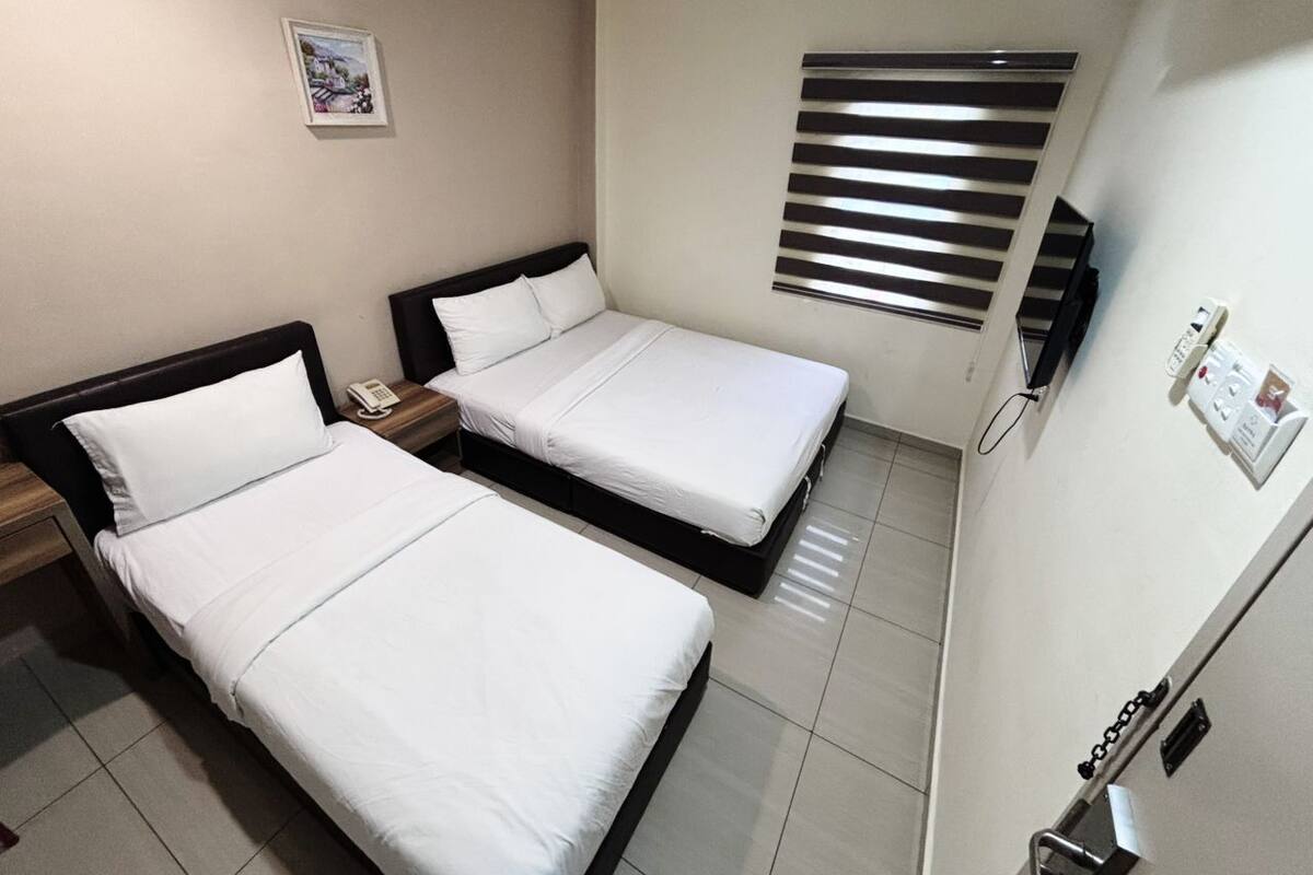 Hotellihuone, jossa on kaksi erillistä sänkyä, yöpöytä, jossa on puhelin, seinään asennettu ilmastointilaite ja ikkuna, jossa on sälekaihtimet.
