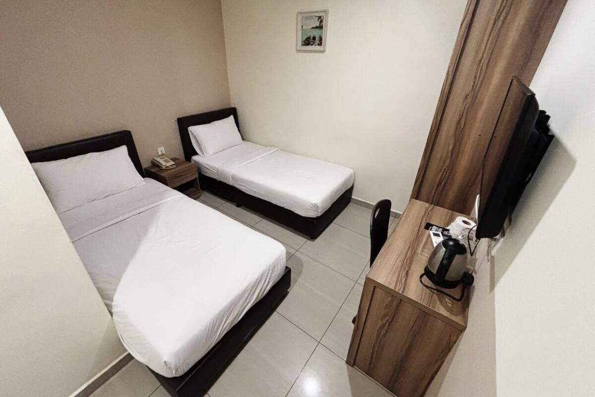 Hotellihuone, jossa on kaksi sänkyä, puinen työpöytä, tuoli, pieni pöytä, puhelin ja televisio.