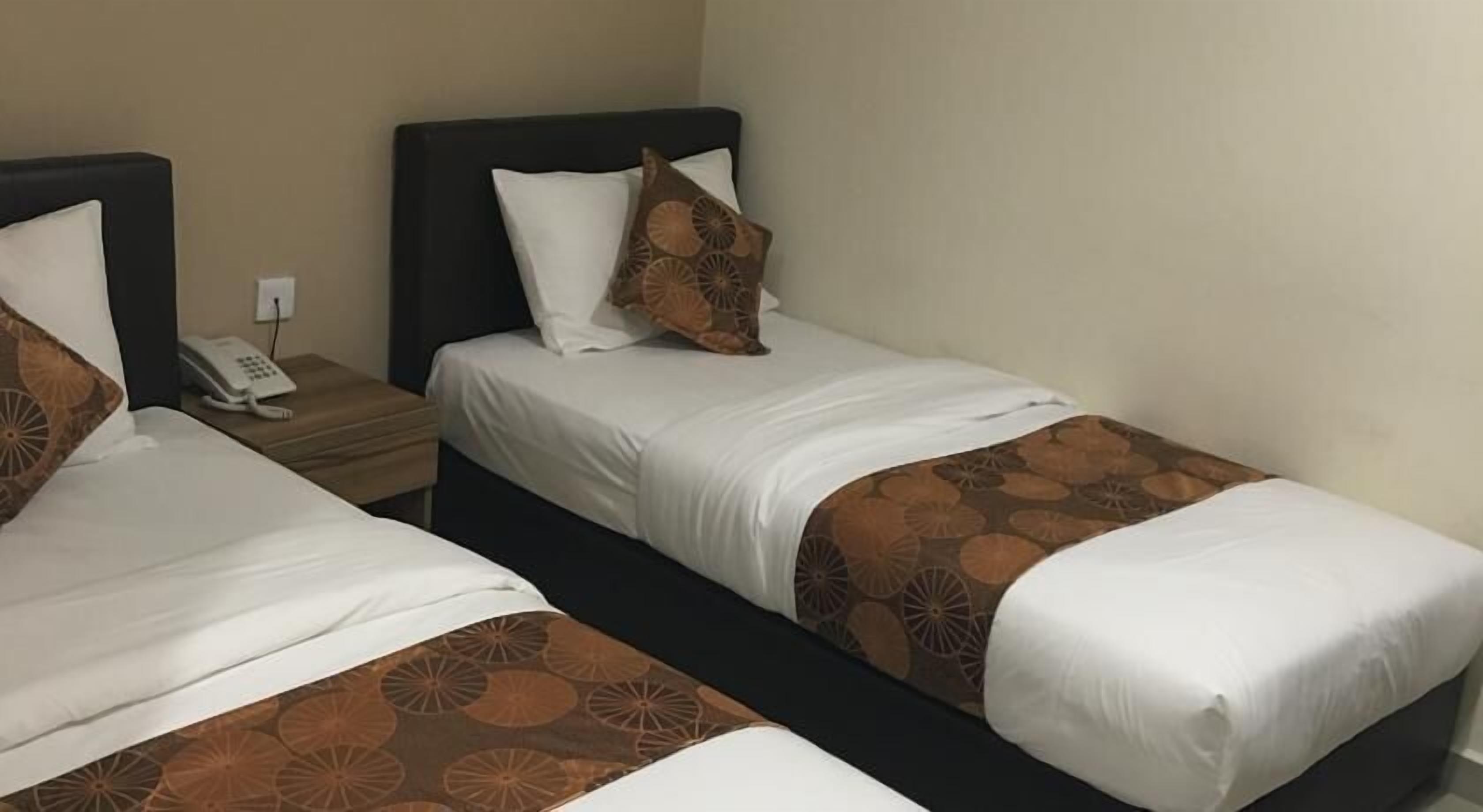 Two single beds with white linens and brown patterned bedspreads in a hotel room.