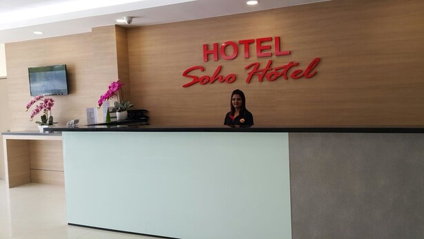 A hotel reception desk with a wooden panel wall, a digital screen, and a receptionist. - SOHO HOTEL (SEMENYIH) SDN. BHD. (Semenyih)