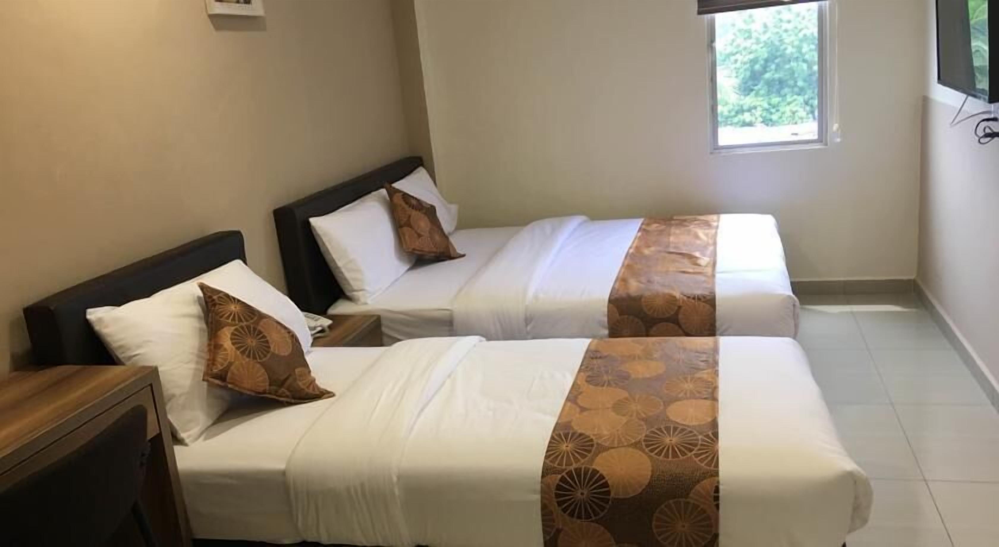 A hotel room with two single beds, each with a pillow and a headboard. There is a window providing natural light and a view of greenery outside.