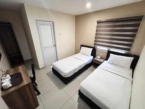 Une chambre d’hôtel avec deux lits simples, un bureau avec une chaise, une petite table avec un téléphone et une tasse, et une porte.