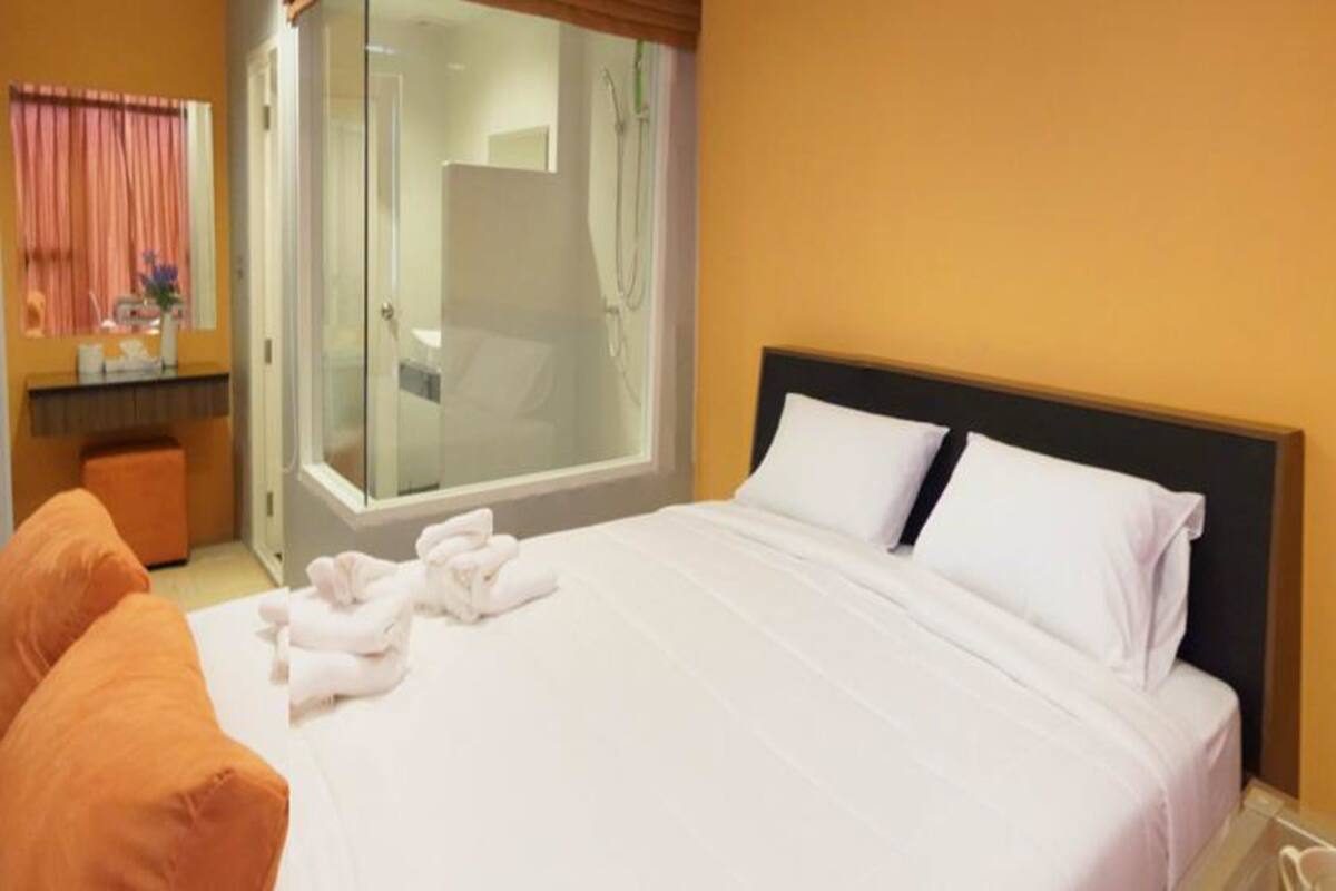 Quarto de hotel com cama, banheiro com porta de vidro e janela com cortinas.