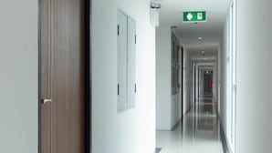 A long, narrow hallway with a wooden door on the left, white walls, and a green emergency exit sign at the end. - La Casa Pattaya (Pattaya)