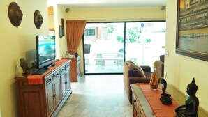 A living room with a TV, a sofa, a coffee table, and a Buddha statue. - Baan Laksee Pool Villa (Pattaya)