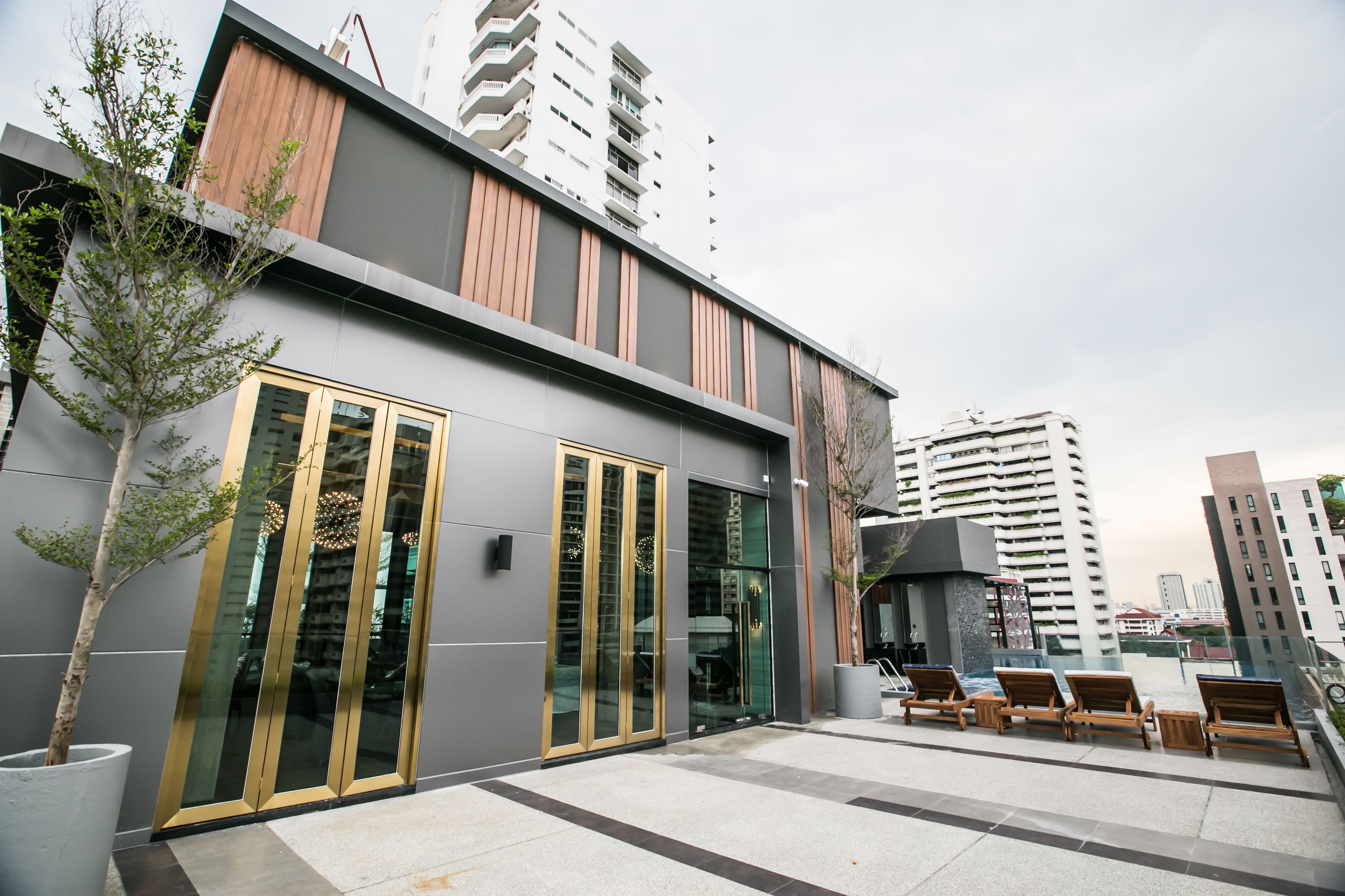 A modern building with large glass doors and a rooftop lounge area with wooden chairs.