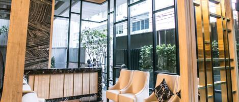 Un vestíbulo moderno con un mostrador de recepción, zona de estar con sofás y sillones, ventanas amplias y conductos de aire acondicionado.