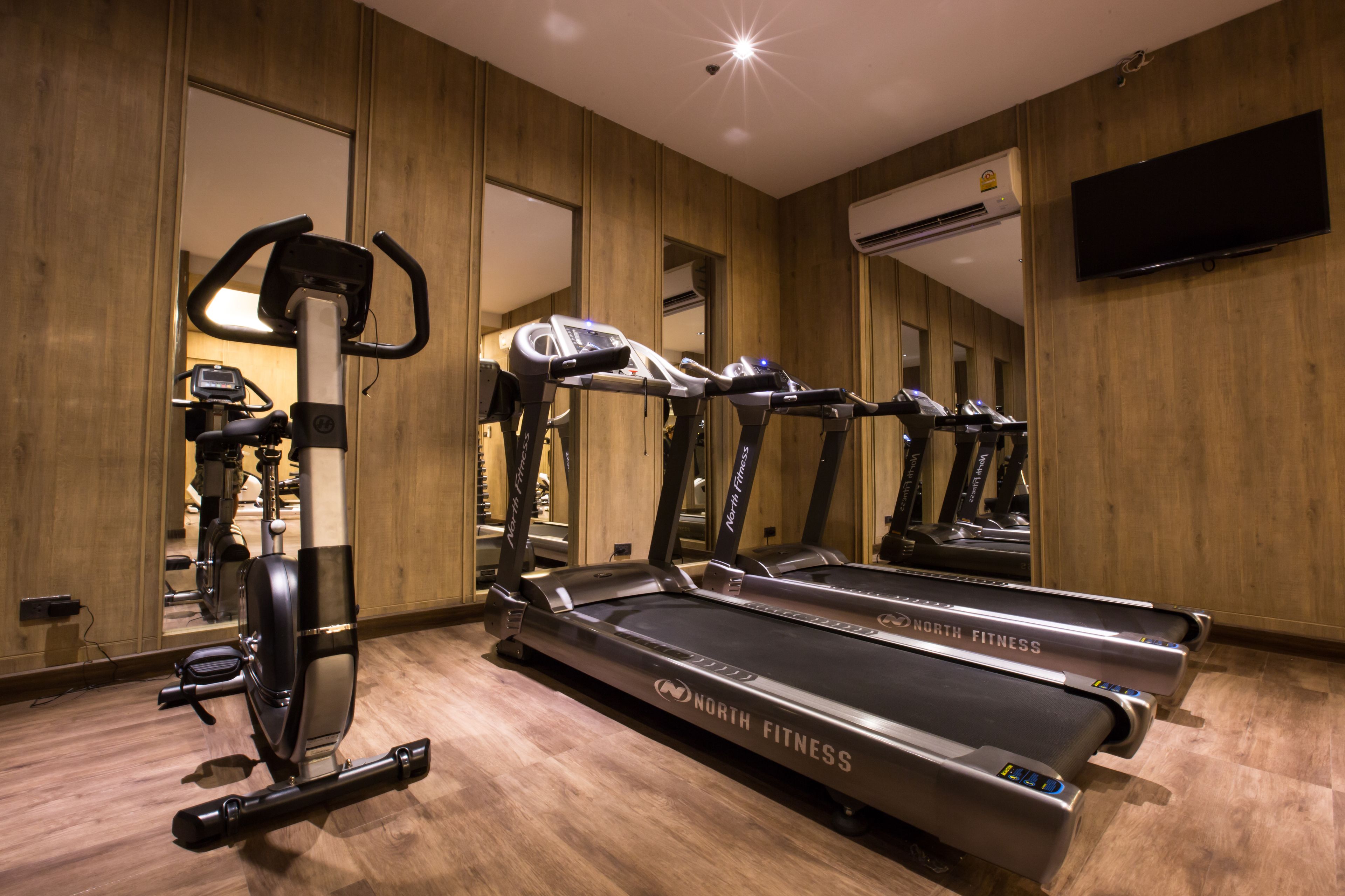 Un gimnasio con cintas de correr, bicicletas estáticas y una pared de espejos.