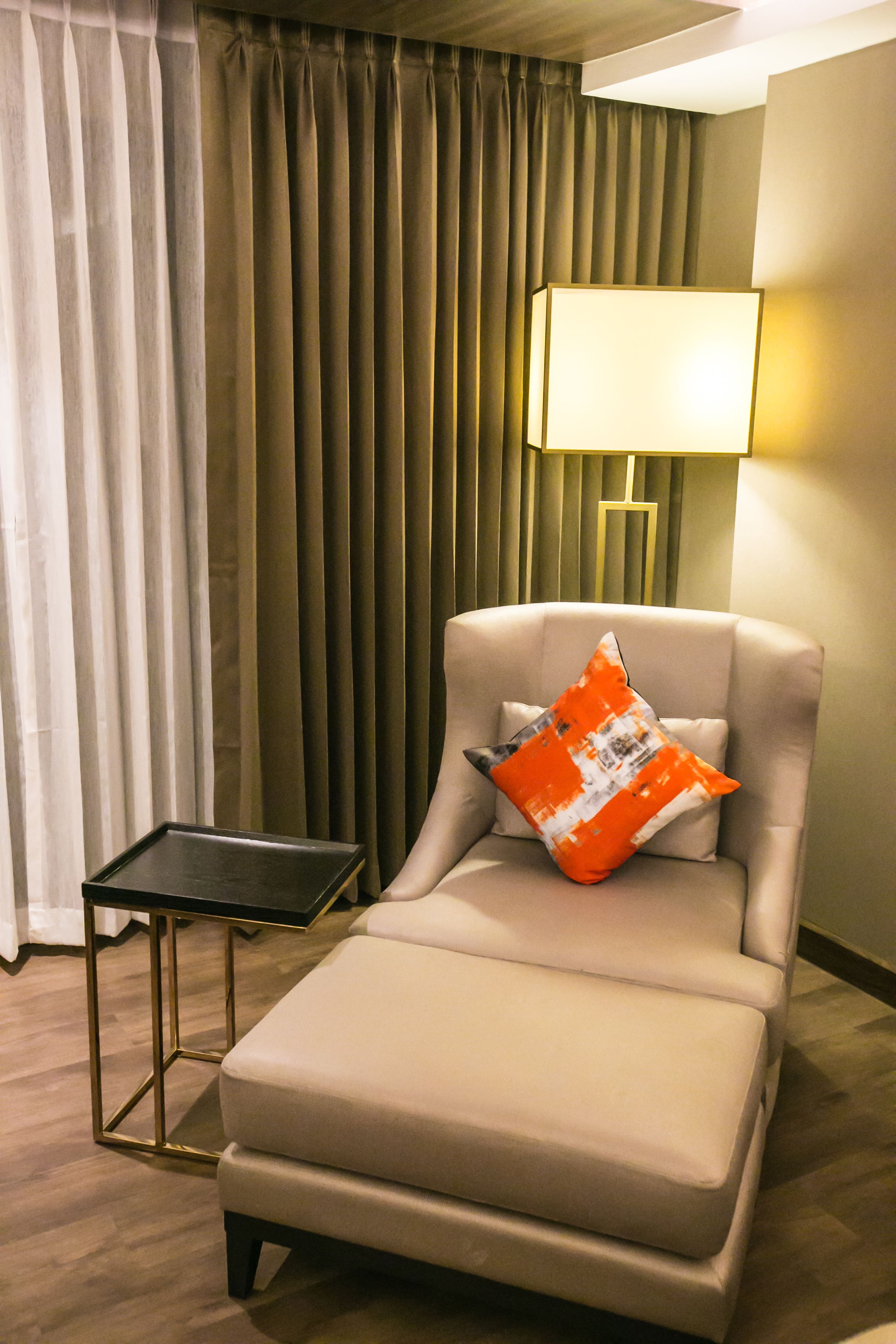 A modern hotel room with a beige sofa, a small side table, and a lamp.