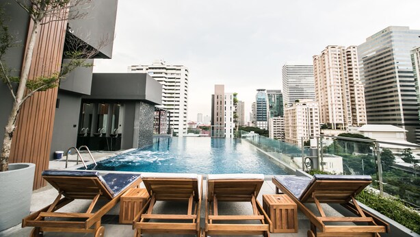 Ein Pool mit Wasserspiegel, der nahtlos in die Skyline übergeht, mit Holzliegen, umgeben von hohen Gebäuden.