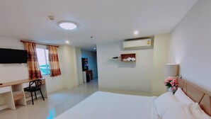 Habitación de hotel con cama, escritorio, silla, televisor, aire acondicionado y un estante pequeño con toallas.