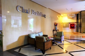 A lobby with a 'Chai Building' sign, a sofa, two armchairs, a small table with a vase, and a patterned floor.