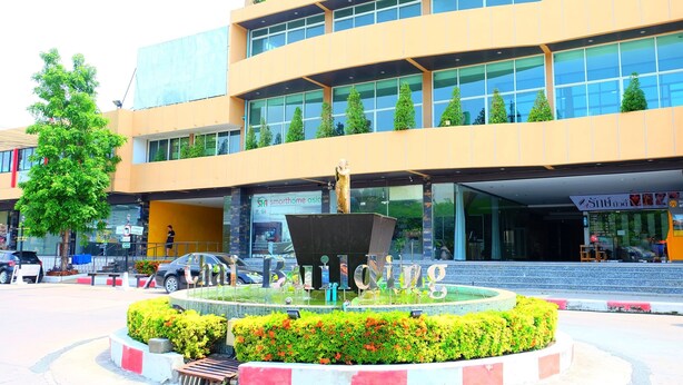 Un edificio moderno con una fuente central, rodeado de un área ajardinada con arbustos y flores.