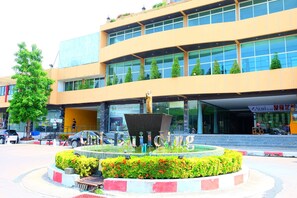 A modern building with a central fountain, surrounded by a landscaped area with bushes and flowers. - Chai Hotel Bangbo (Bang Bo)