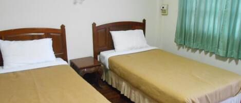 Una habitación con dos camas individuales, cabeceros de madera, ropa de cama blanca, una mesita de noche pequeña y una cortina verde.