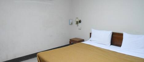 A hotel room with a bed, a nightstand, an air conditioning unit, and a wall-mounted lamp.