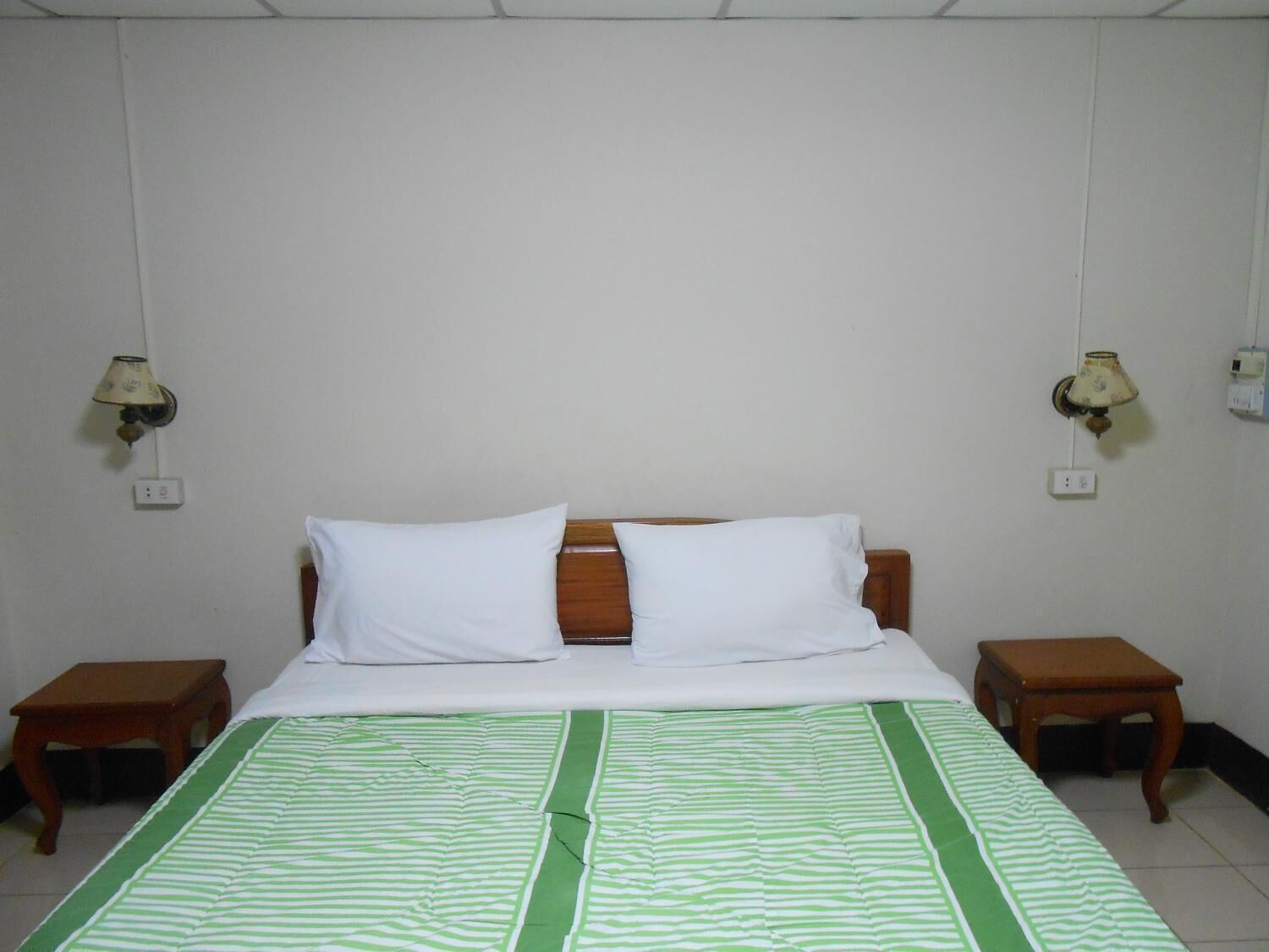 A hotel room with a bed, two nightstands, and two wall-mounted lamps.