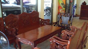 A dining area with a wooden table and ornate chairs, a fan, and a motorcycle visible through the window. - Souvanna Hotel 2 (Vientiane)
