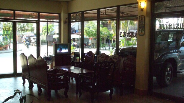 A restaurant with large windows, a television, and a seating area with wooden furniture. - Souvanna Hotel 2 (Vientiane)