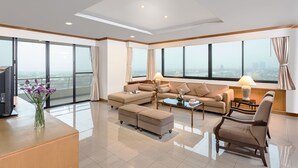 Amplia sala de estar con un ventanal grande, un conjunto de sofás, una mesa de centro y un televisor sobre un mueble de madera.