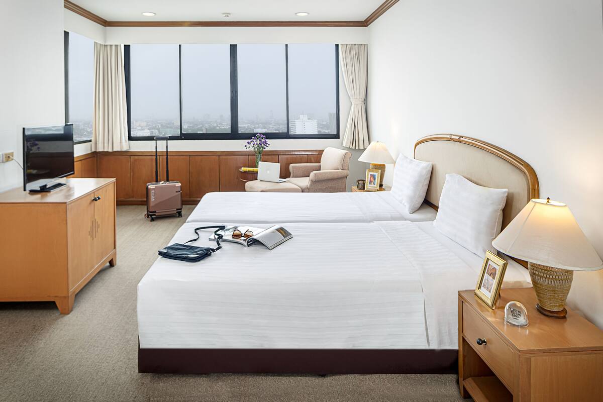 Une chambre d’hôtel avec un grand lit, un bureau avec une télévision, une chaise, une lampe et une vue sur la ville grâce à de grandes fenêtres.