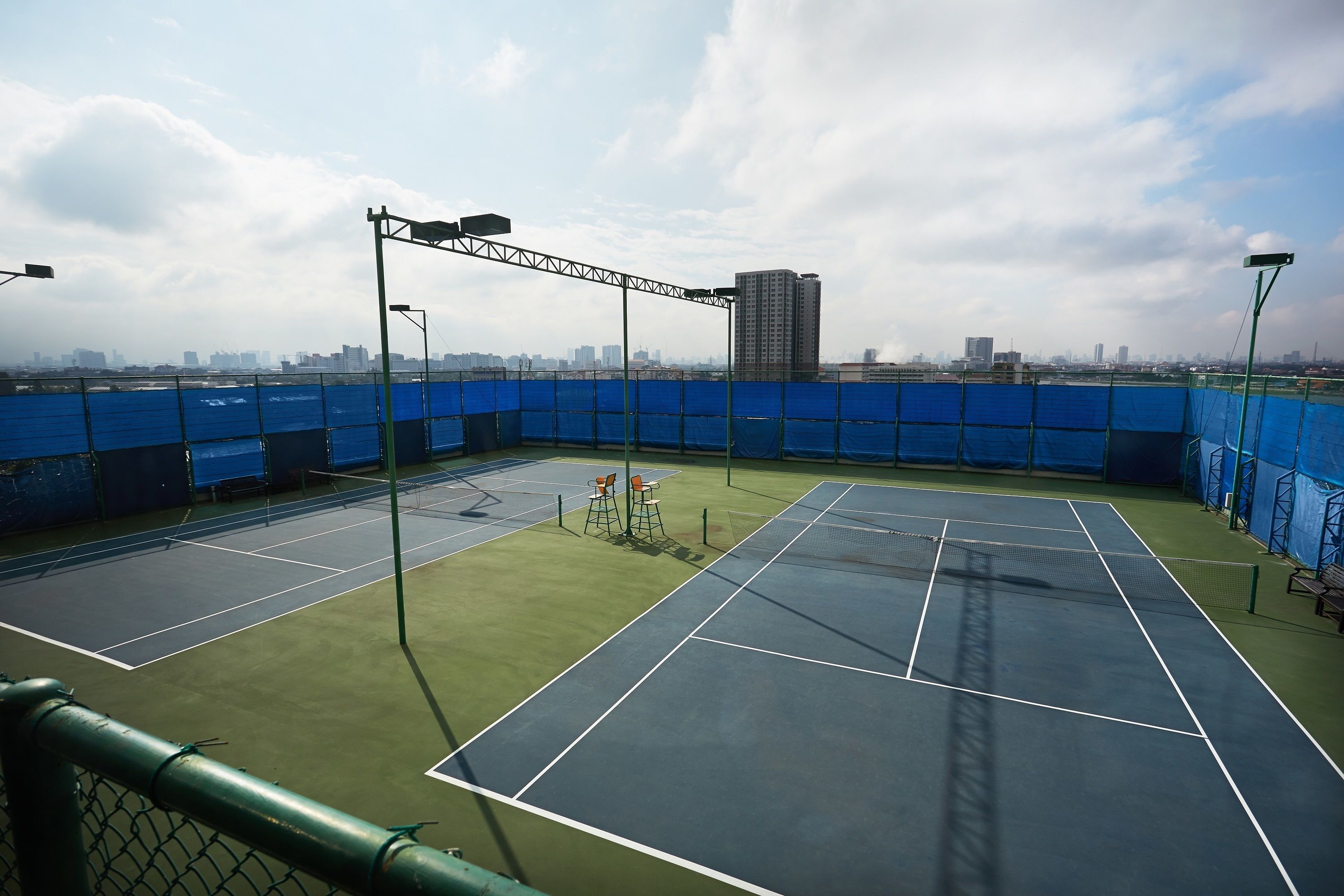 Een overdekte tennisbaan met meerdere velden, een net en een uitzicht op een stadshemel in de verte.